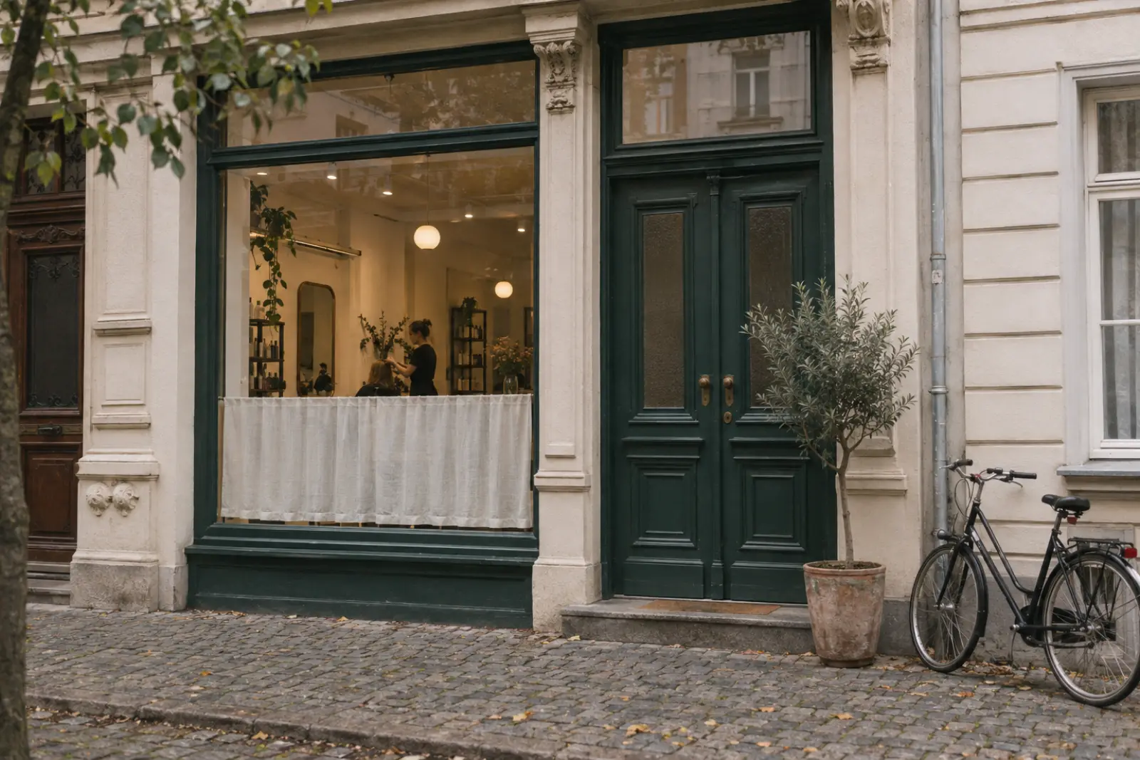 Eingang des Salons: grüne Holztür, Schaufenster und Olivenbaum